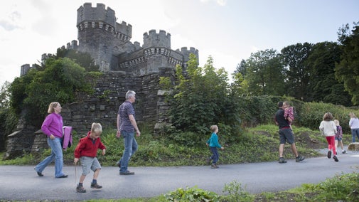 A family pass under Wray Castle on a path during a walk in Cumbria